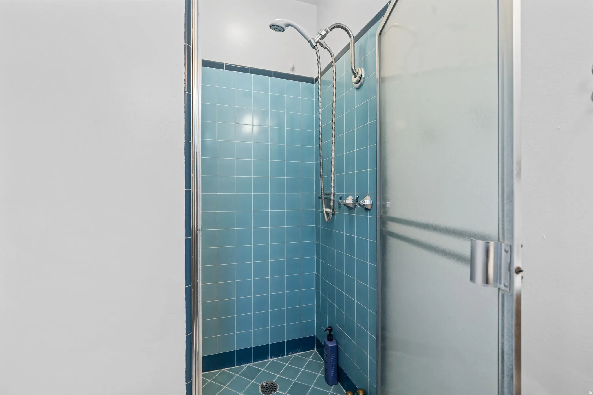Shower enclosure featuring blue tiled walls and floor, chrome fixtures, and a frosted glass door with a metal frame