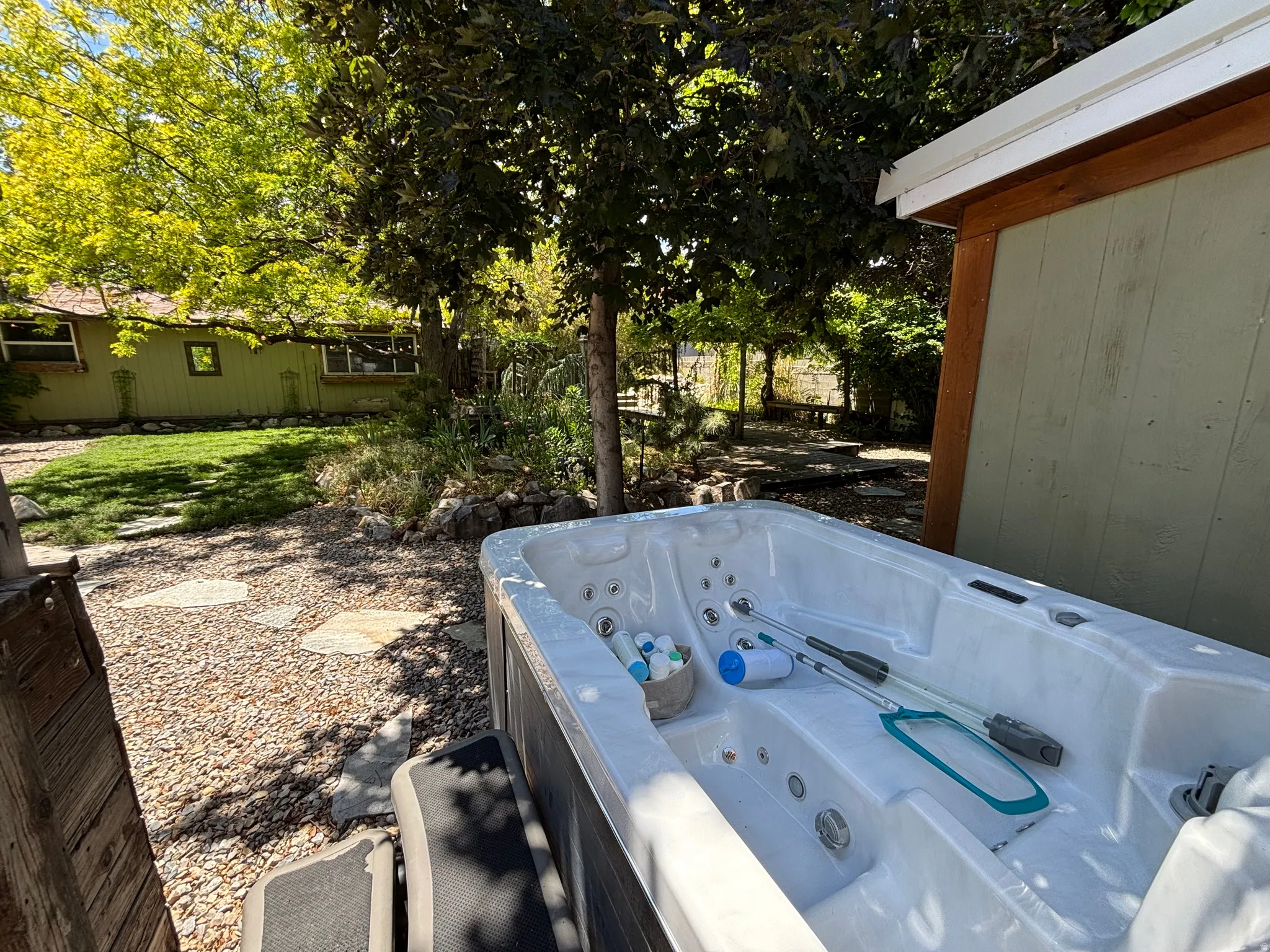 Outdoor spa setup adjacent to deck and garden bedroom, set within a landscaped backyard featuring mature trees, and a stone pathway