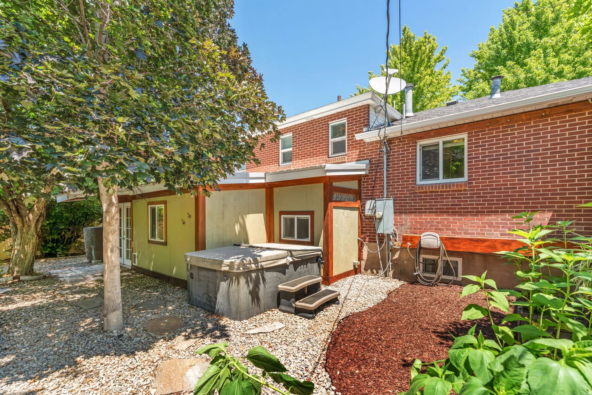 Private outdoor area featuring a hot tub with built-in steps, mature trees, and a mix of gravel and mulch landscaping
