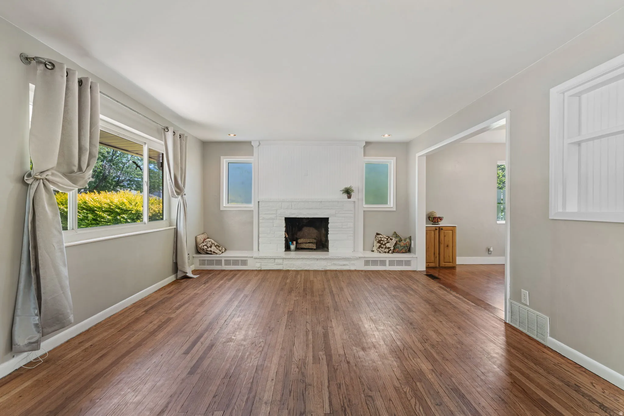 Expansive living area featuring hardwood flooring, a white-painted brick fireplace, and multiple windows