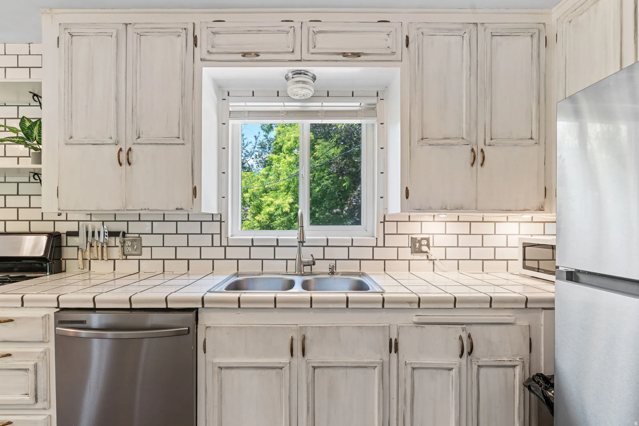 Kitchen featuring white painted cabinetry, white tile countertops, subway tile backsplash, and a stainless steel double basin sink