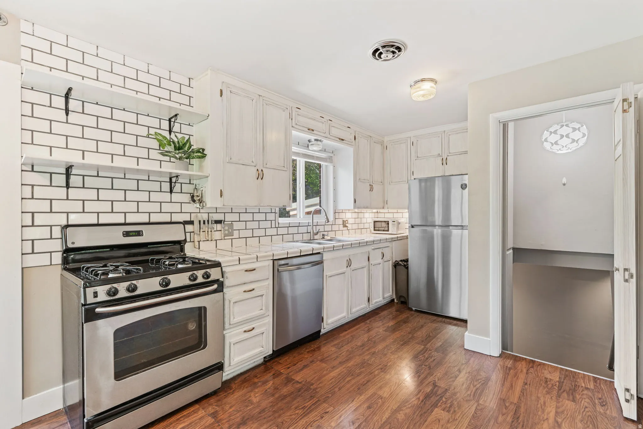 Kitchen featuring wood-finish flooring, white subway tile backsplash, white cabinetry, stainless steel appliances, and some open shelving