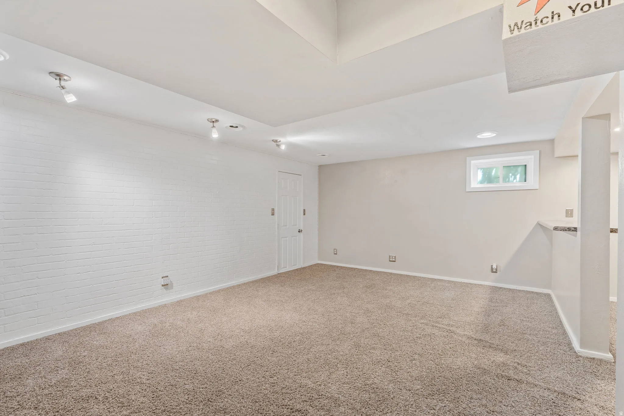 Carpeted room with a white painted brick accent wall and track lighting