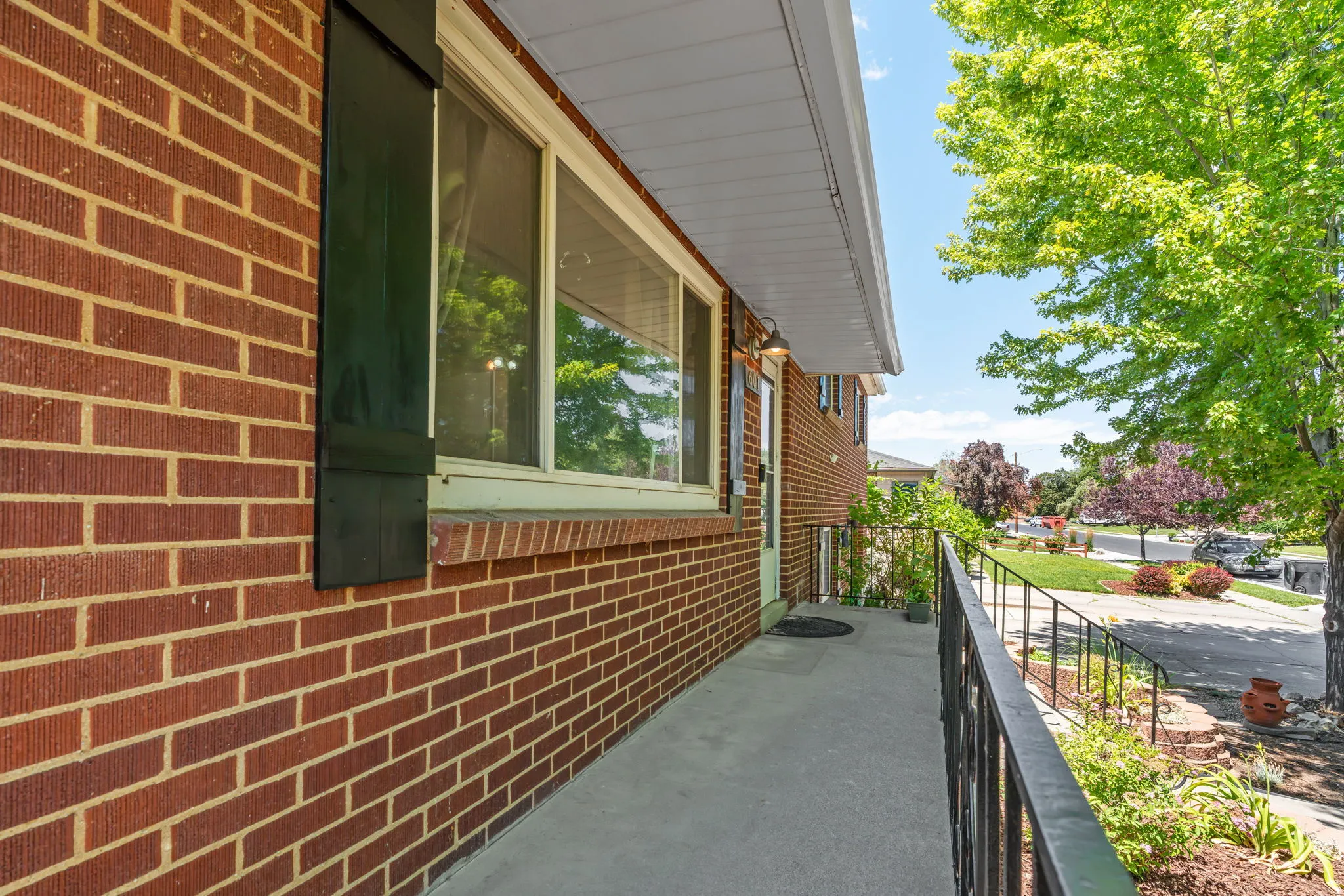 Brick exterior featuring a window with dark shutters, a concrete porch, and a black metal handrail