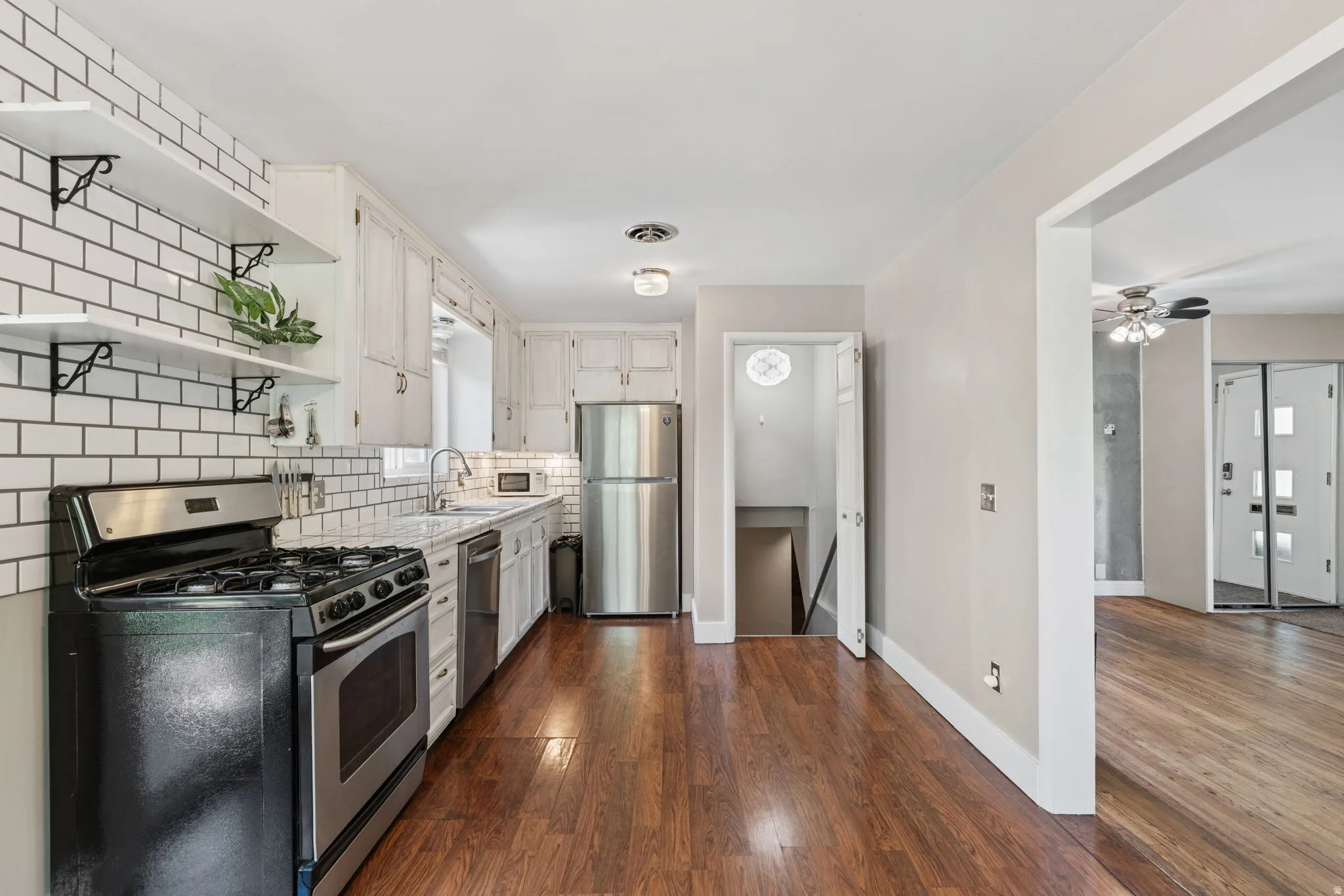 Kitchen featuring white subway tile backsplash, open shelving, wood-finish flooring, white cabinetry, and stainless steel appliances
