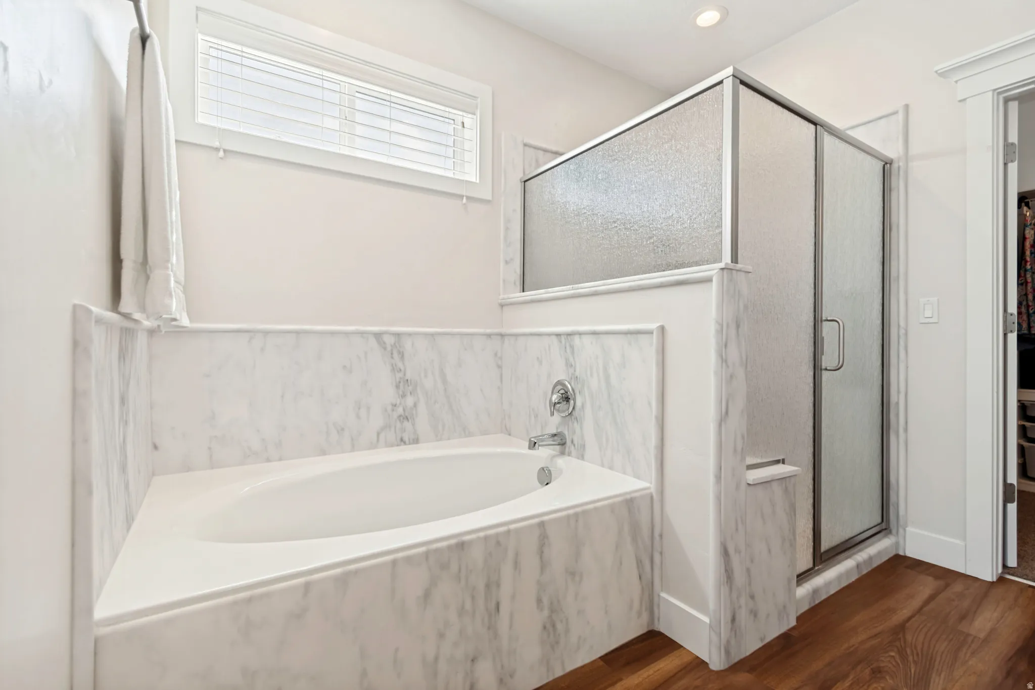 Bathroom featuring a built-in soaking tub with a polished chrome faucet, a glass-enclosed shower with a textured panel, and wood-finish flooring