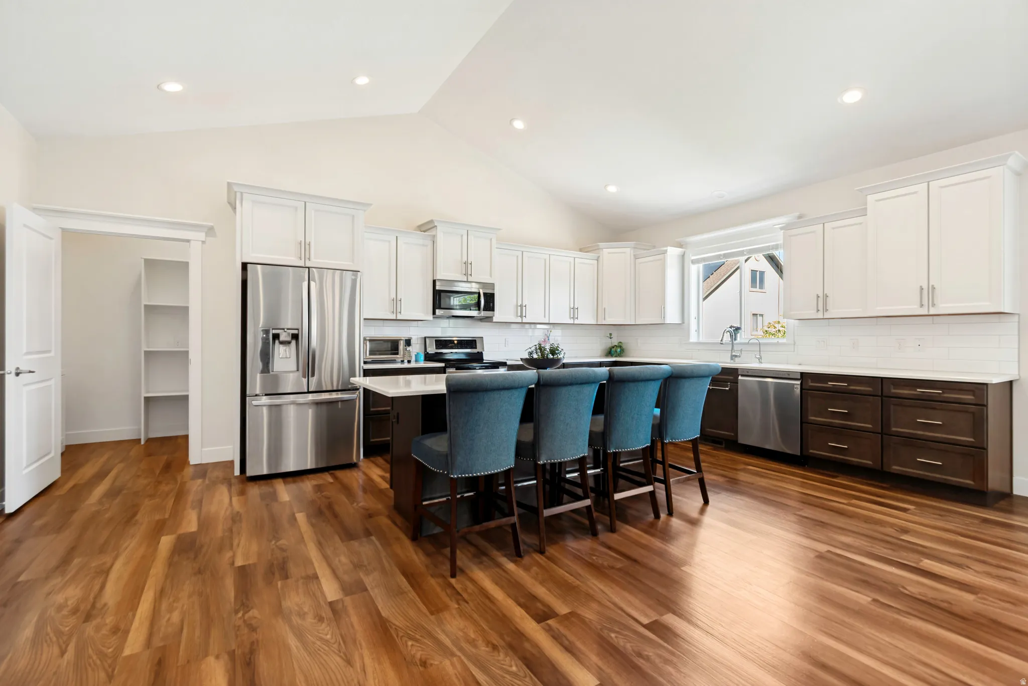 Open-concept kitchen featuring wood-finish flooring, a vaulted ceiling with recessed lighting, and a kitchen island with seating