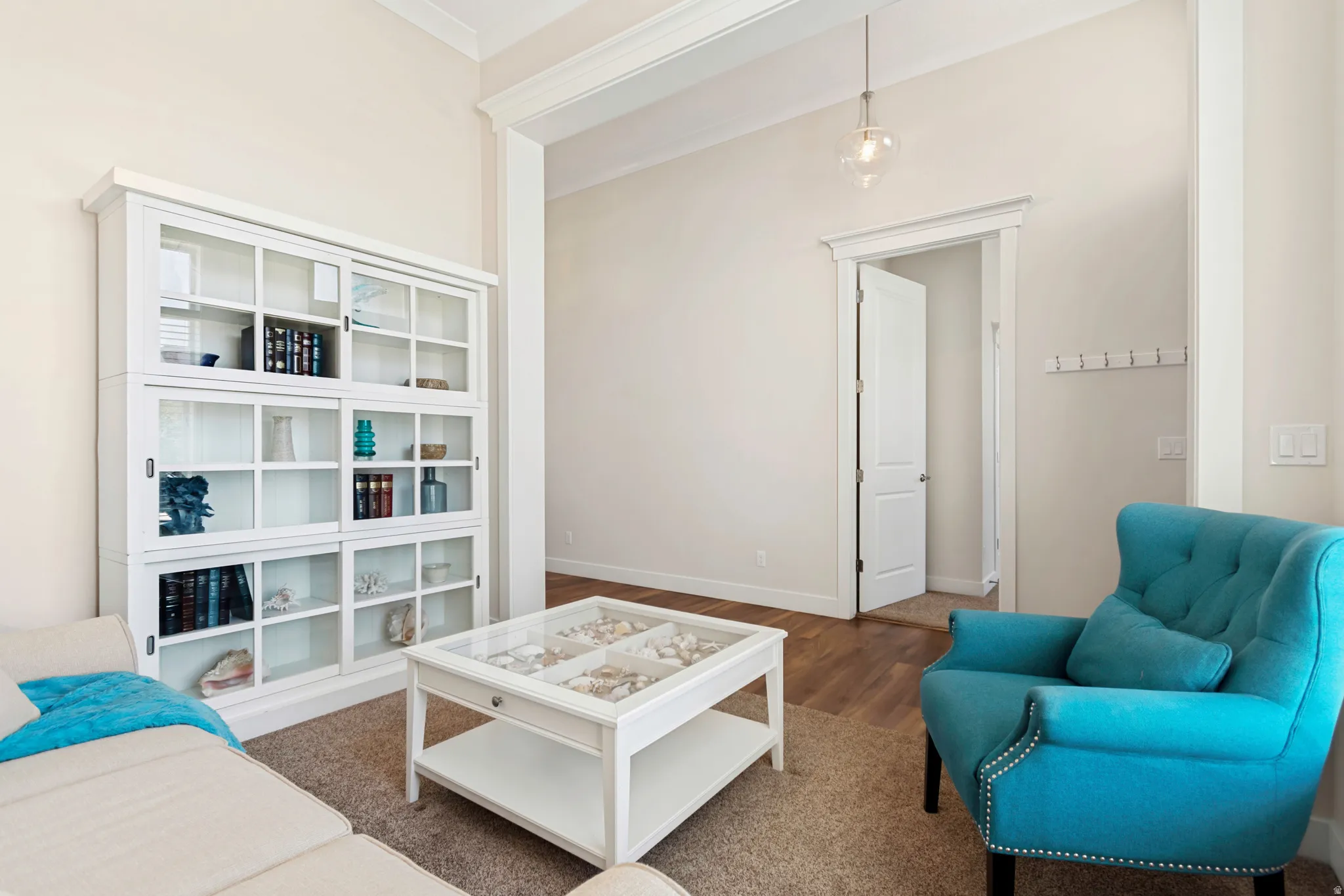 Living area featuring high ceilings with crown molding, a built-in display cabinet with sliding glass doors, and a decorative pendant light fixture