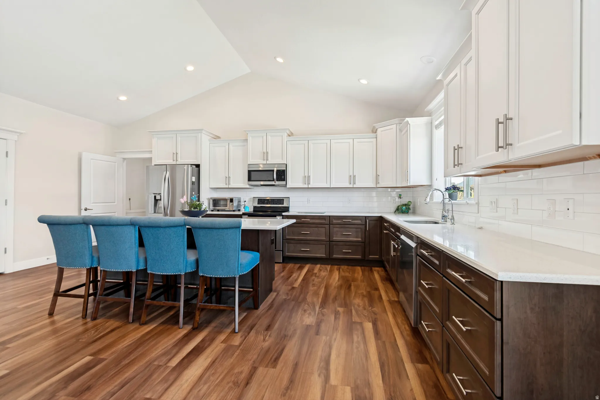 Spacious kitchen featuring wood-finish flooring, a vaulted ceiling, white upper cabinetry, dark lower cabinetry, and a central island with countertop seating