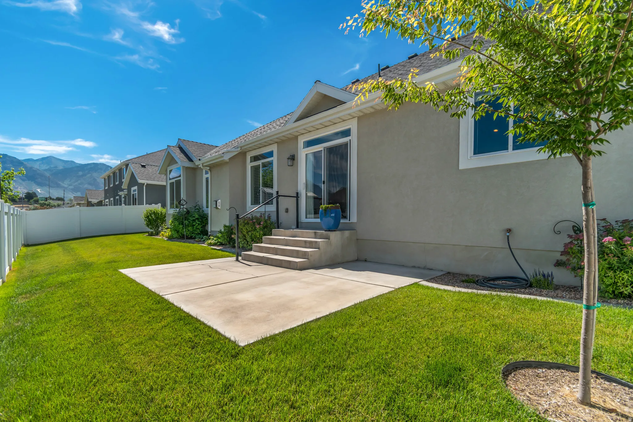Expansive green lawn with a white vinyl fence, concrete patio, and mature trees