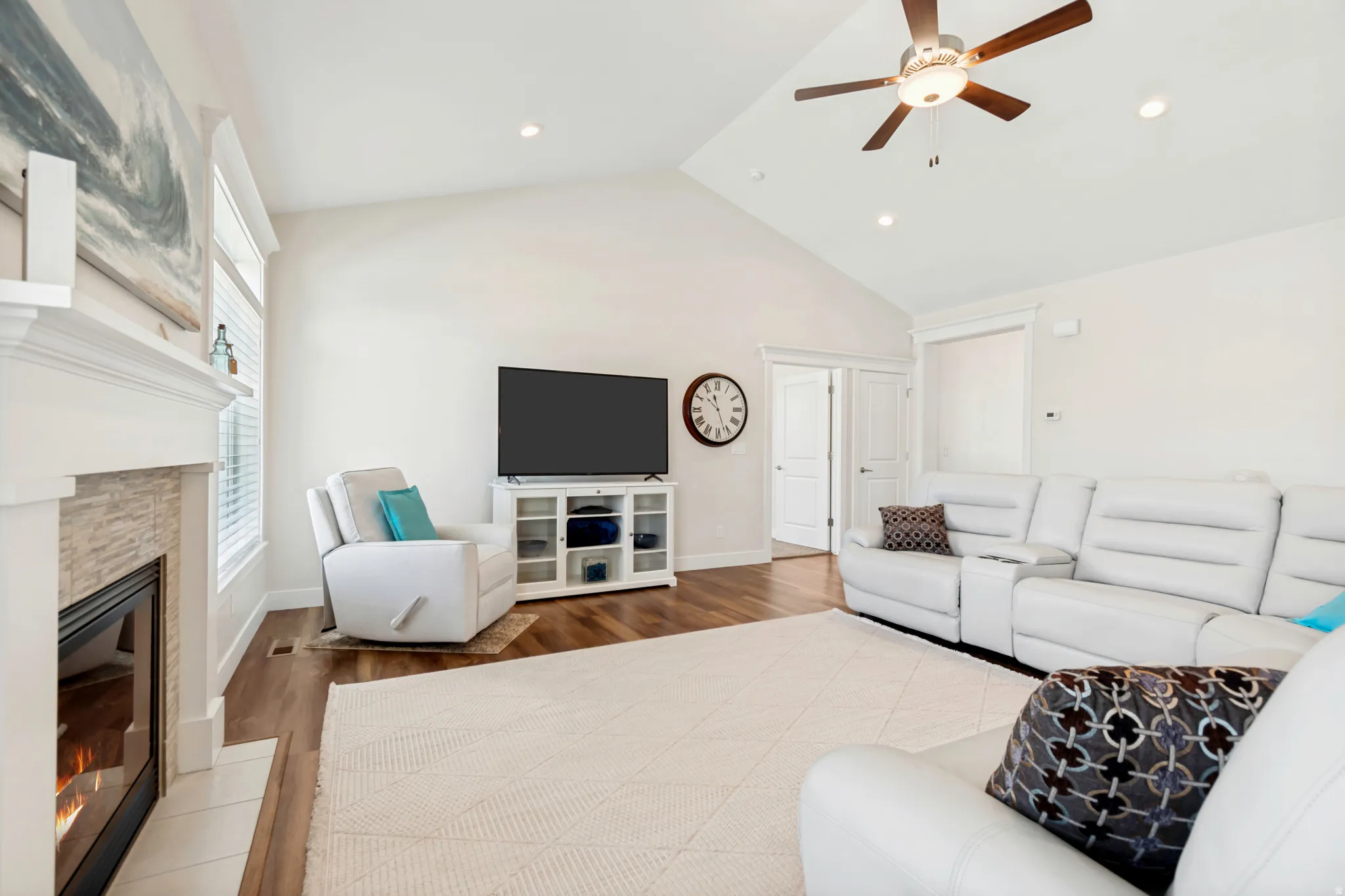 Spacious living area featuring vaulted ceilings, recessed lighting, wood-finish flooring, a contemporary ceiling fan, and a fireplace with a stone-clad surround and white mantel