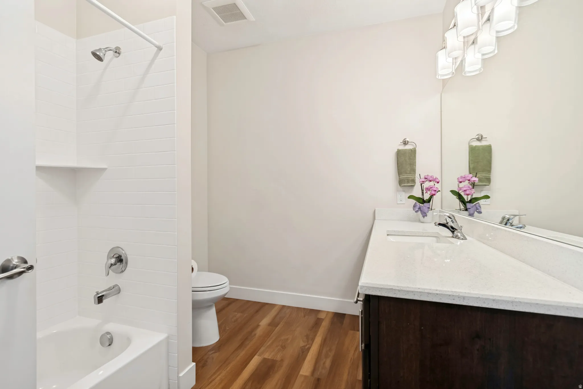 Bathroom featuring a white subway tile shower surround with integrated shelf, a white bathtub with chrome fixtures, a dark wood-finish vanity with a white countertop, and a modern light fixture above the vanity mirror