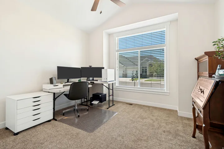 Vaulted ceiling room featuring a large window with blinds, neutral carpet flooring, and a ceiling fan