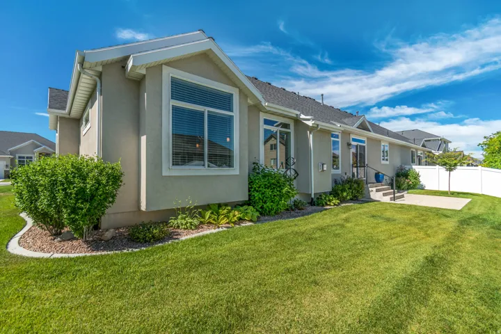 Expansive lawn area featuring a concrete patio, white vinyl fencing, and mature landscaping