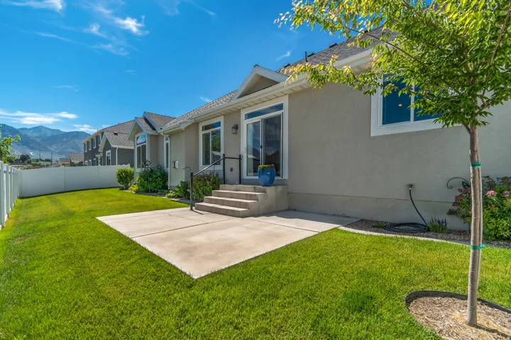 Expansive green lawn with a white vinyl fence, concrete patio, and mature trees