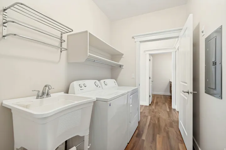 Dedicated utility room featuring wood-finish flooring, a white utility sink with a chrome faucet, wall-mounted drying racks, and built-in shelving