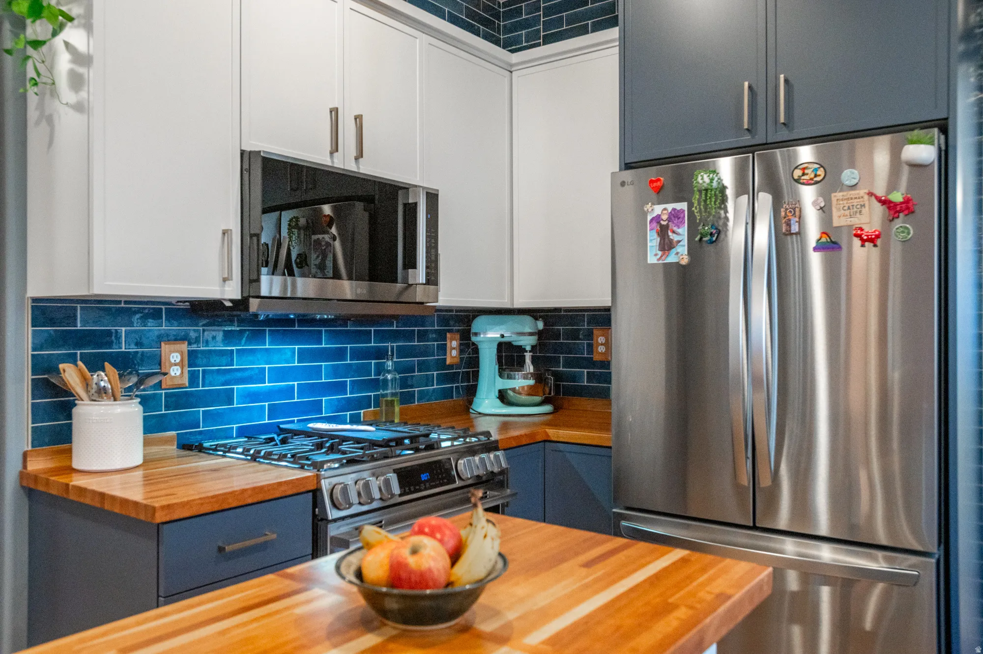 Kitchen featuring blue subway tile backsplash, wood-finish countertops, stainless steel appliances, a gas range, and two-tone cabinetry