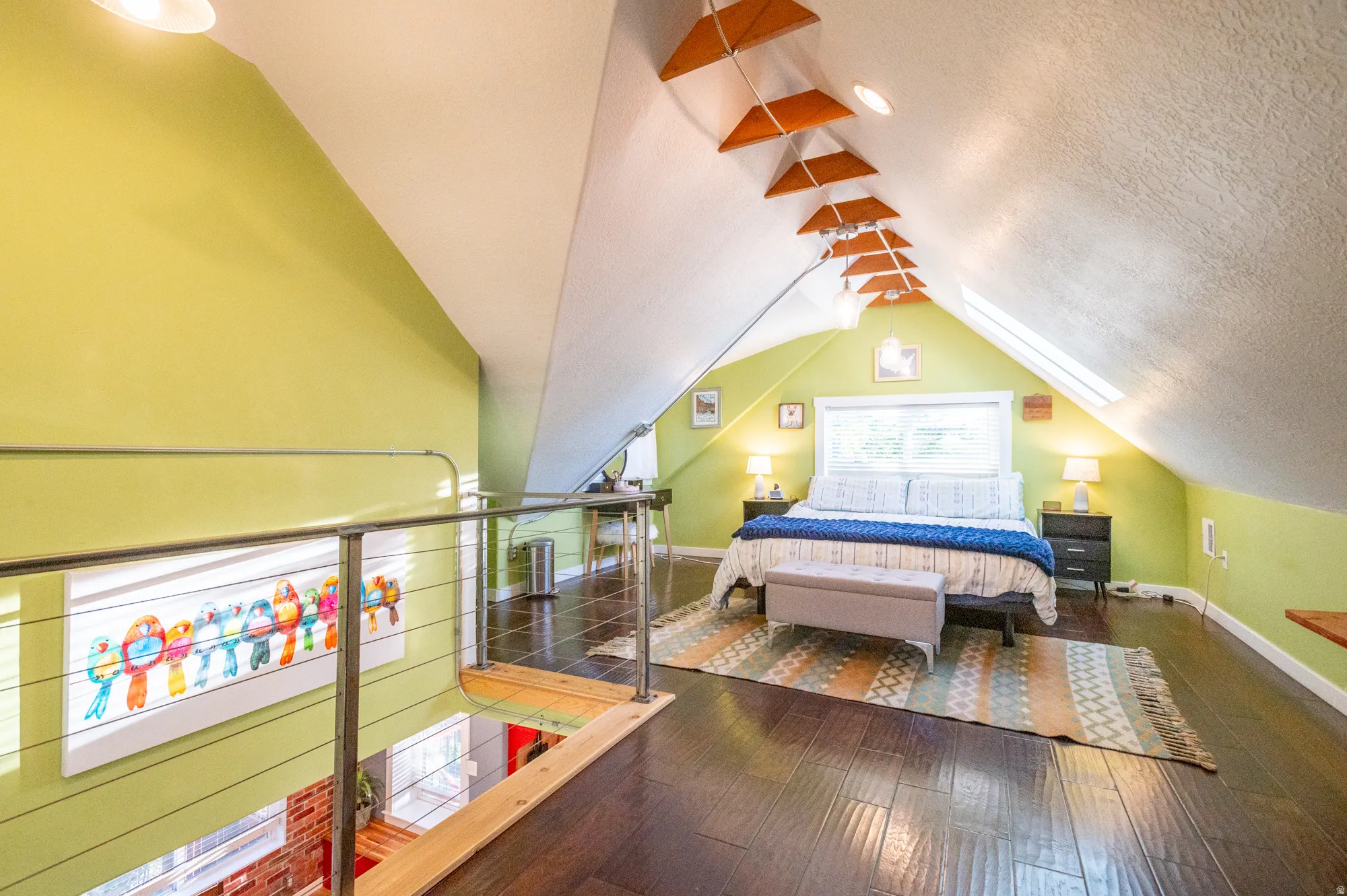 Loft space featuring wood-finish flooring, a vaulted ceiling with skylights, accent lighting, and a metal cable railing overlooking the lower level
