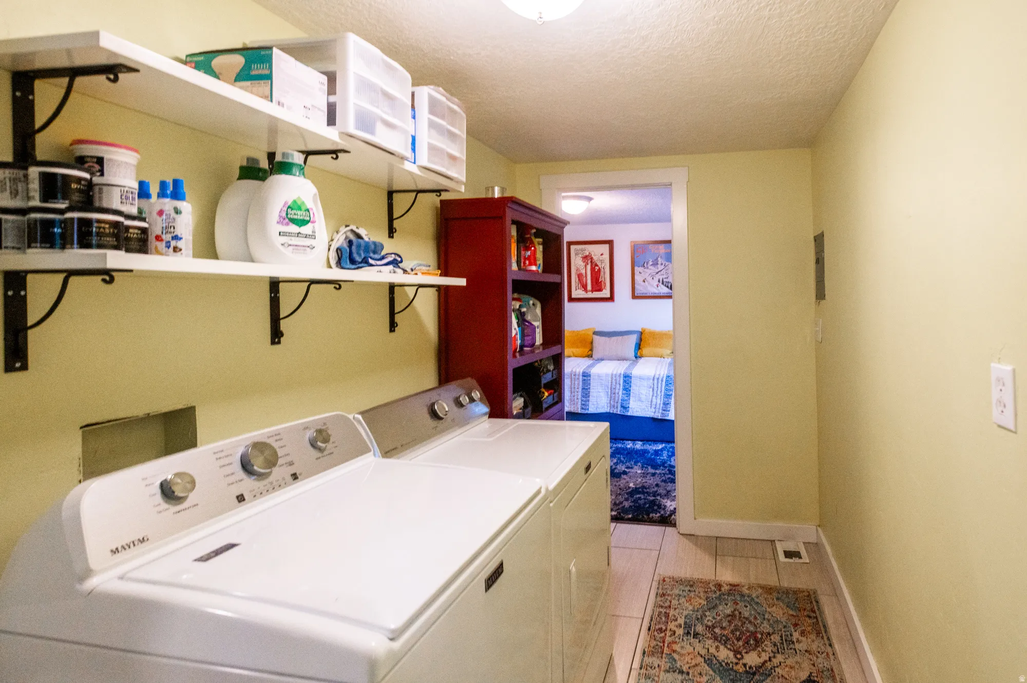 Laundry area featuring a side-by-side washer and dryer, open shelving with decorative brackets, a red wooden storage unit, and tile flooring