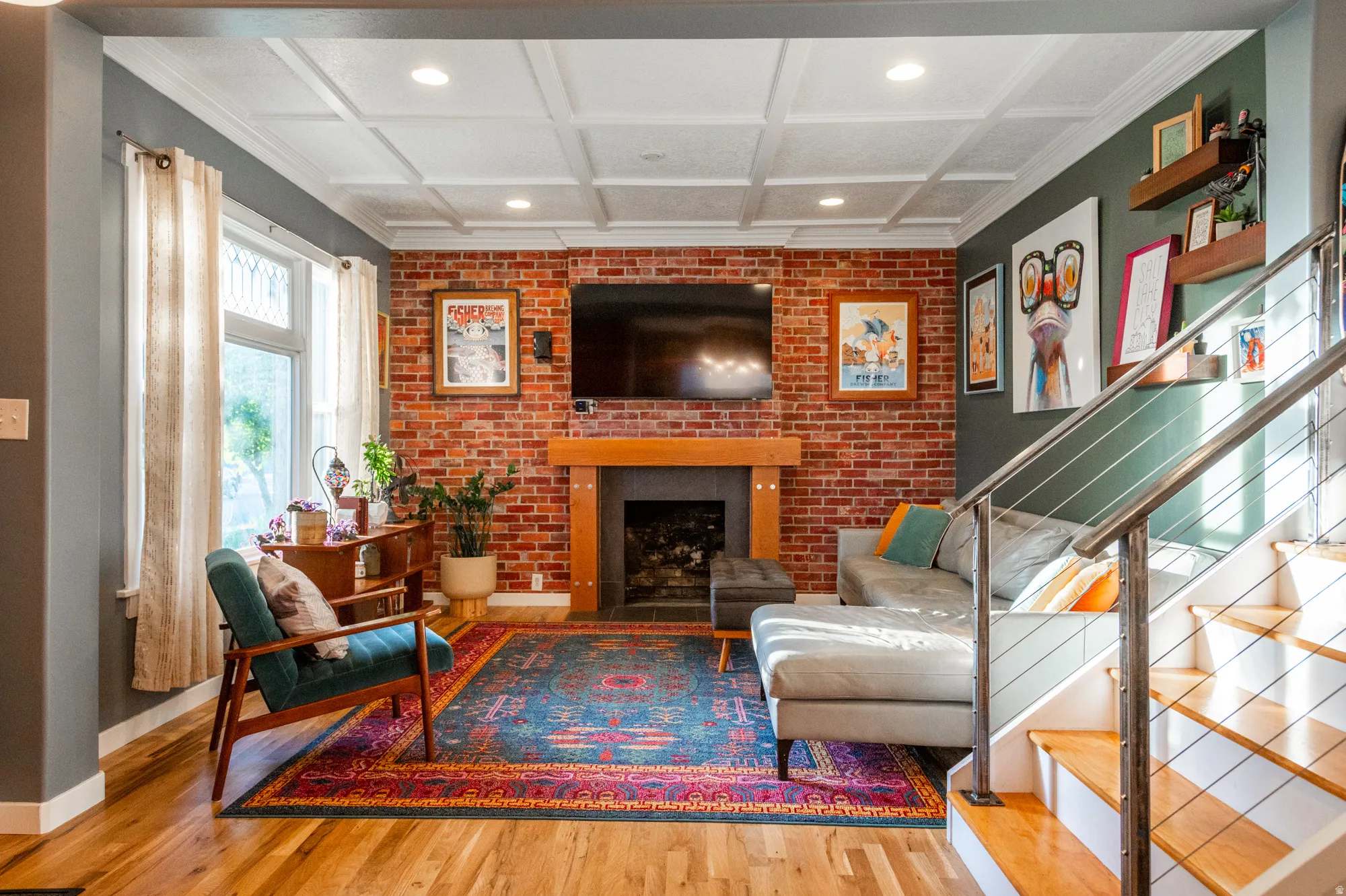Living area featuring a brick accent wall, fireplace with wooden mantel, wood-finish flooring, coffered ceiling with recessed lighting, and a modern cable railing staircase