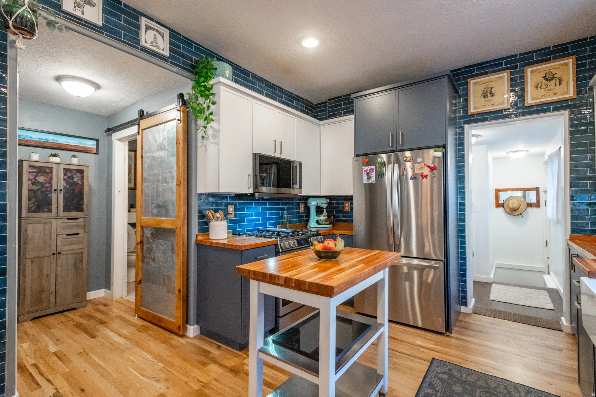 Kitchen featuring wood-finish flooring, two-tone cabinetry, and an exposed brick accent wall