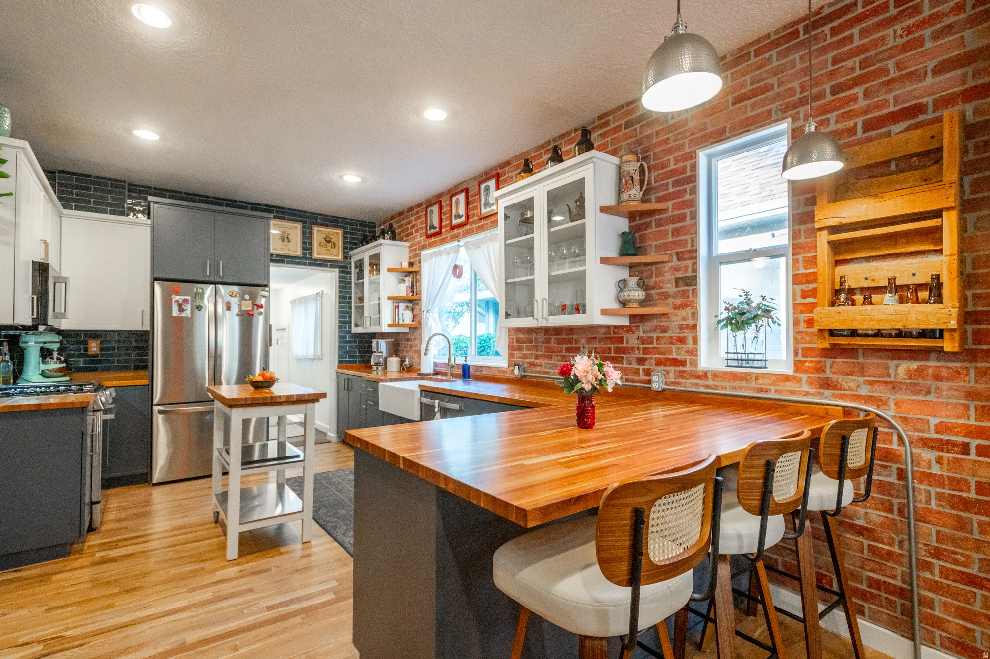 Exposed brick wall kitchen featuring wood-finish countertops, a farmhouse-style sink, stainless steel appliances, and wood-finish flooring