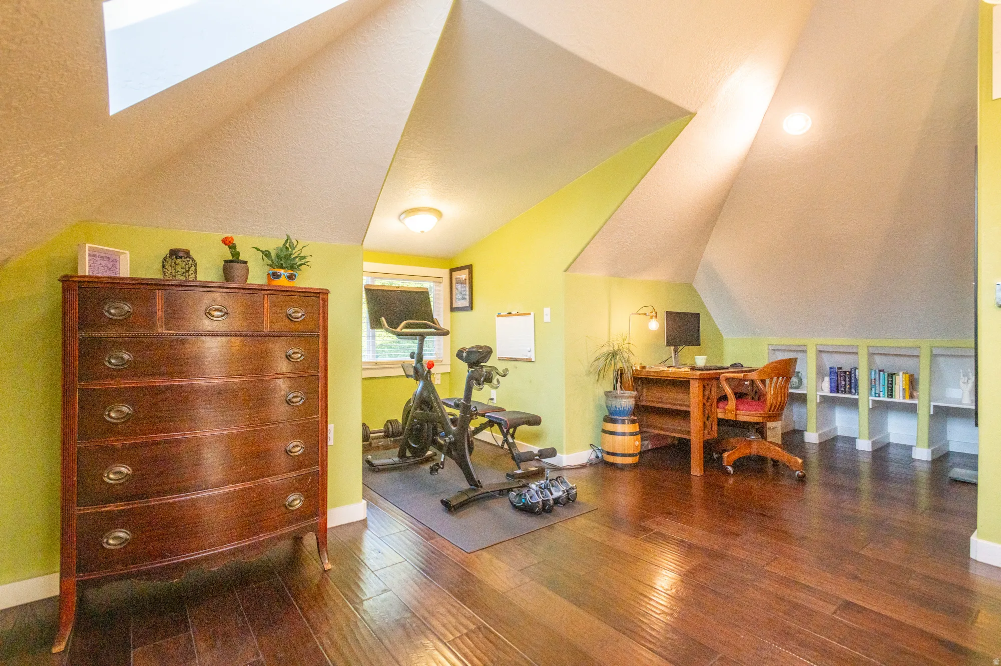 Attic conversion featuring rich wood-finish flooring, bright green accent walls, and angled ceilings with skylights