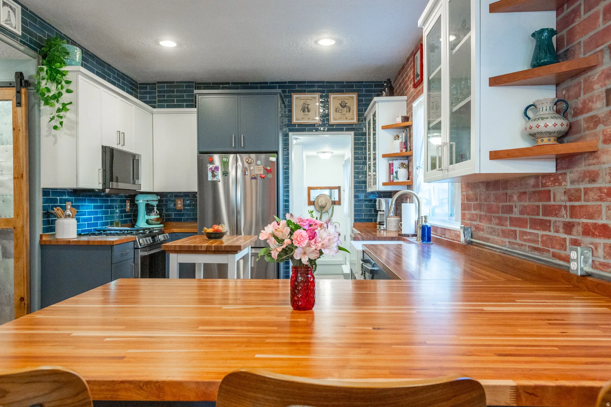 Spacious kitchen featuring extensive butcher block countertops, a contrasting blue subway tile backsplash, and a mix of white and gray cabinetry
