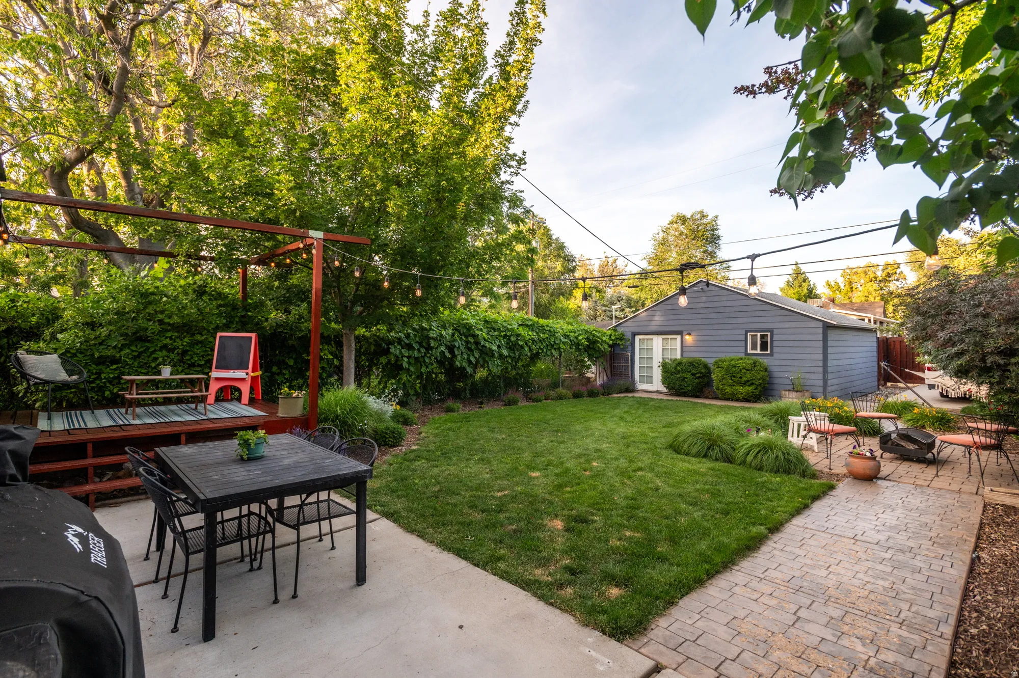 Expansive backyard featuring a lush lawn, concrete patio, and a separate raised wood deck