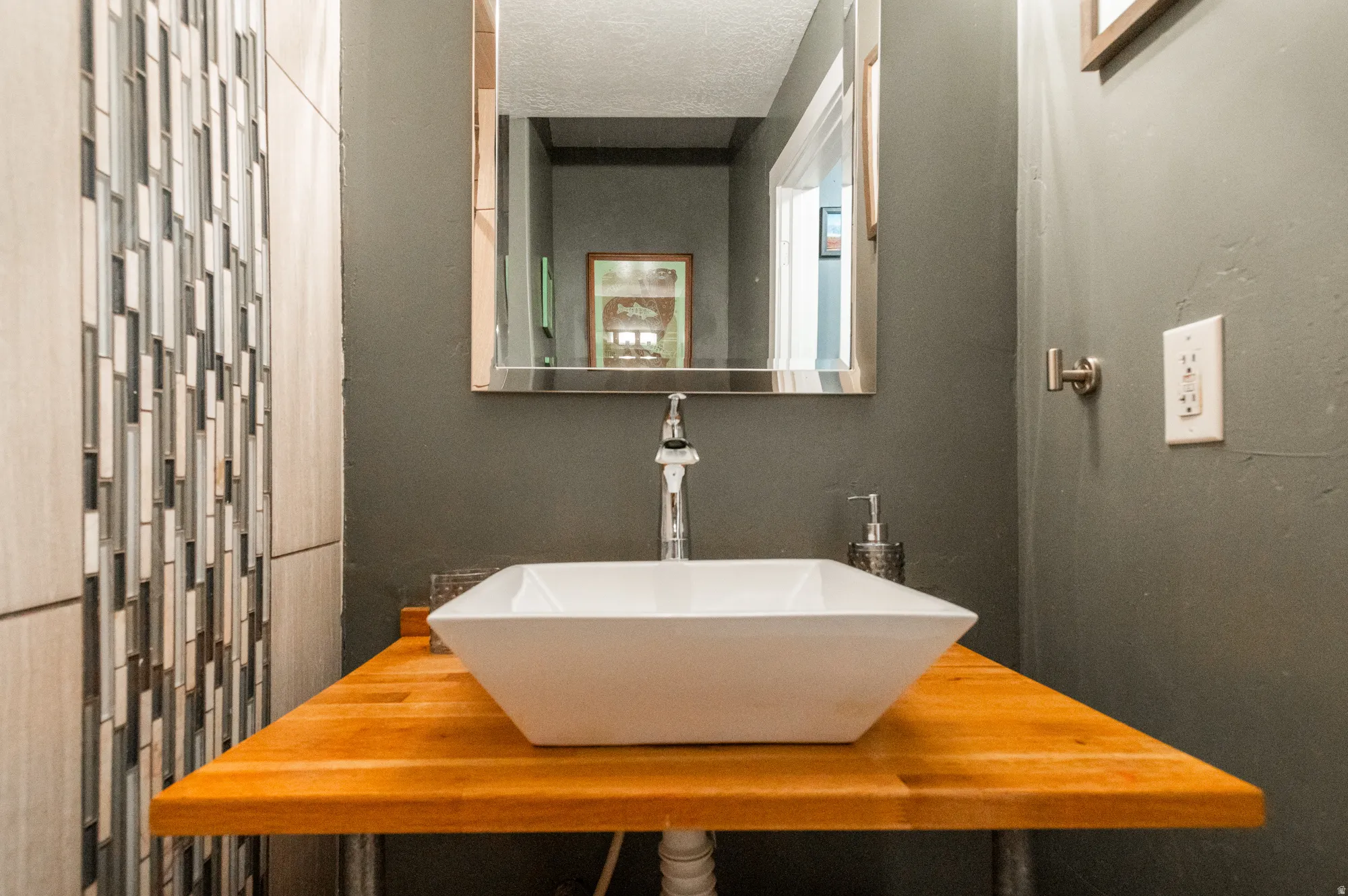 Vessel sink with a wood-finish countertop, brushed metal faucet, and a wall-mounted mirror with a polished frame
