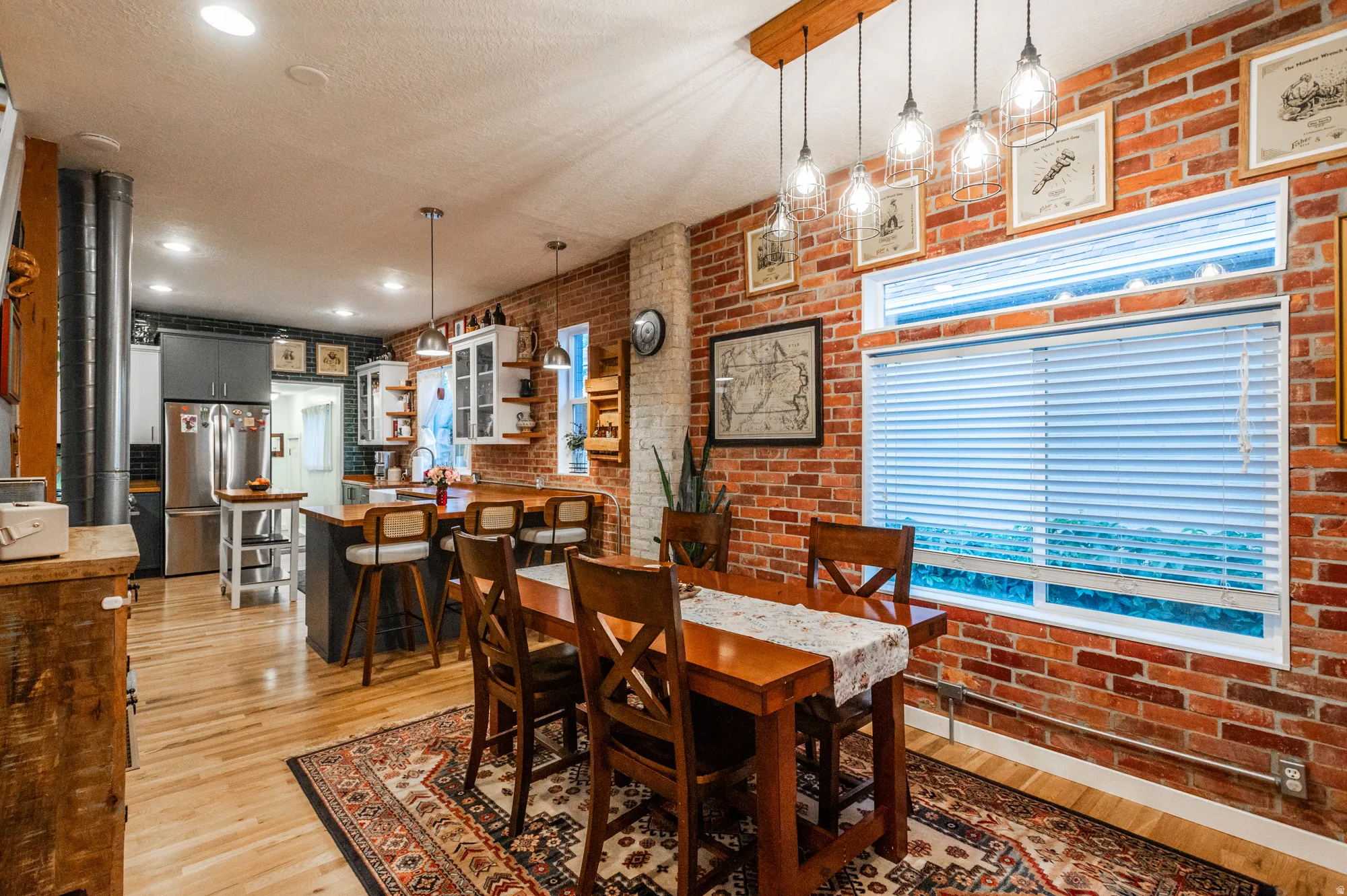 Open-concept living space featuring exposed brick walls, wood-finish flooring, and a kitchen with stainless steel appliances