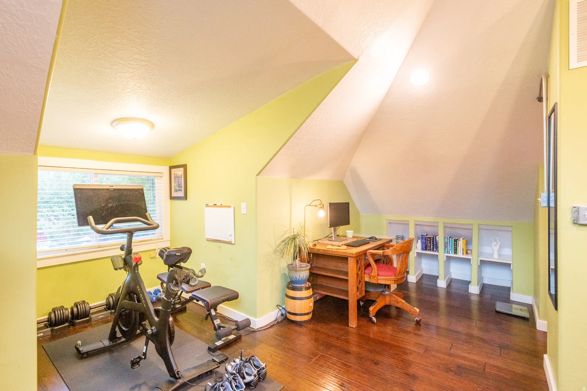 Attic room featuring hardwood flooring, sloped ceilings, and recessed built-in shelving
