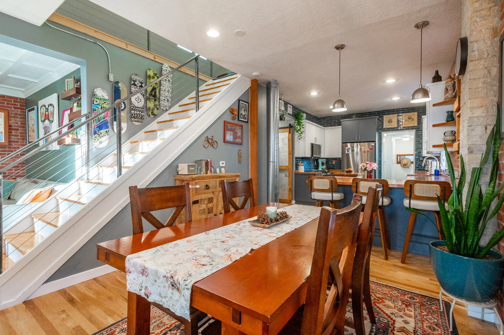 Open-concept dining area featuring wood-finish flooring, a contemporary staircase with metal railings, recessed lighting, and exposed brick accents