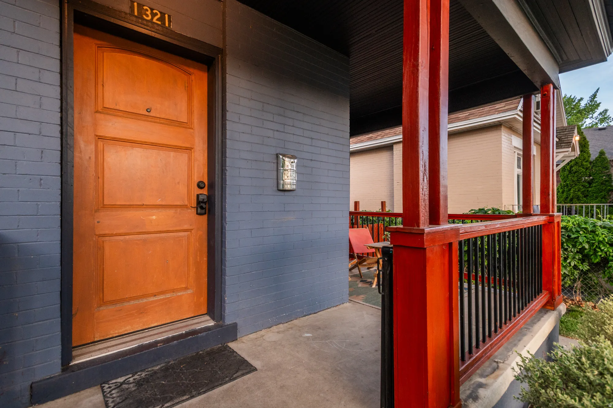Inviting front porch featuring a paneled wood entry door, brick exterior, concrete porch flooring, and a vibrant red railing