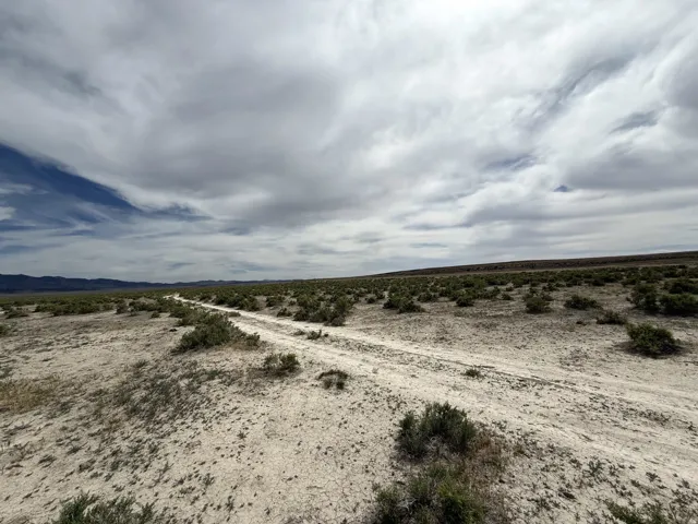 Expansive undeveloped land featuring a dirt path, sparse desert vegetation, and distant mountains under a broad sky