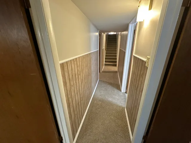 Hallway with wood-finish wainscoting, carpet flooring, and wall-mounted lighting fixtures