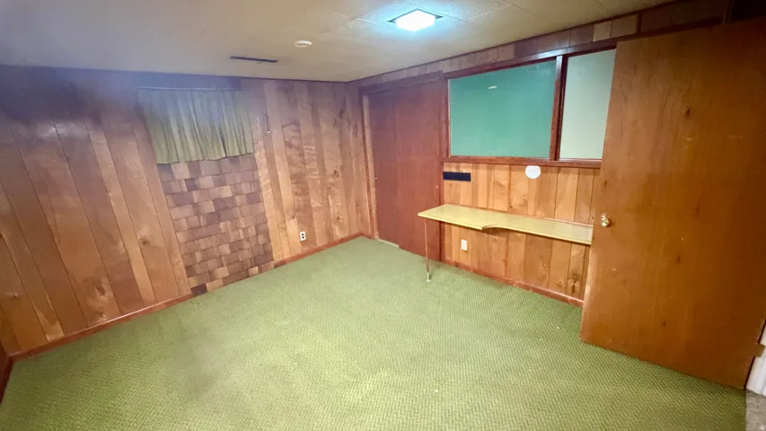 Paneling walls with an integrated desk, green carpeting, and a flush-mount ceiling light