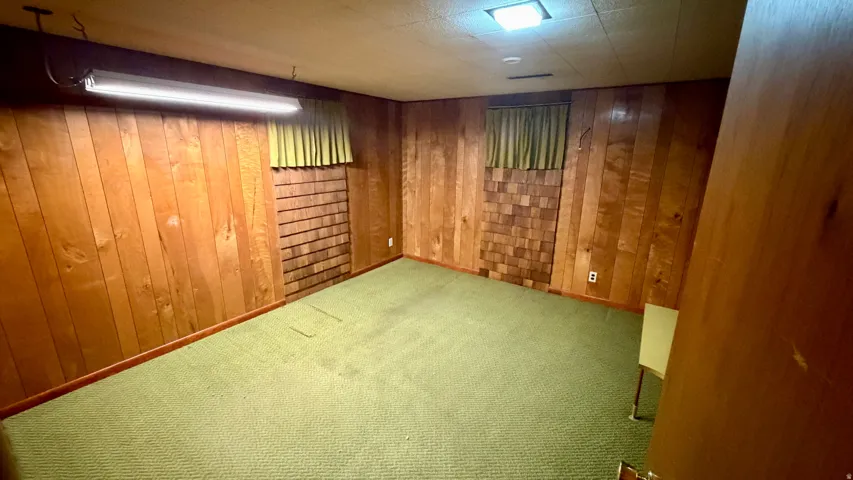 Room featuring wood paneling, green carpet flooring, and a drop ceiling with recessed lighting