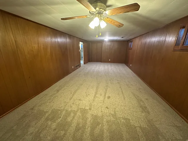 Spacious room with wood-paneled walls and neutral carpeting