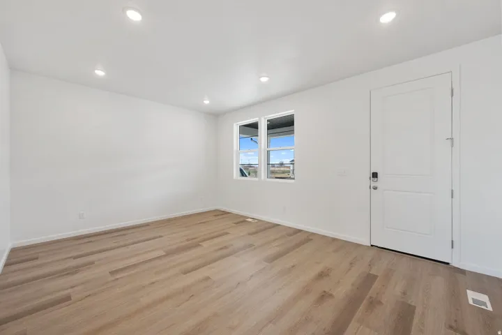 Bright room featuring wood-finish flooring, recessed lighting, and a white paneled door with contemporary hardware