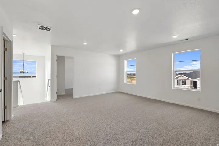 Spacious room featuring neutral carpeting, recessed ceiling lighting, multiple windows, and crisp white walls