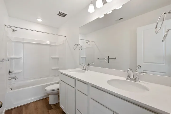Bathroom featuring a dual-sink vanity with white cabinetry, a large mirror, a shower-tub combination, and wood-finish flooring