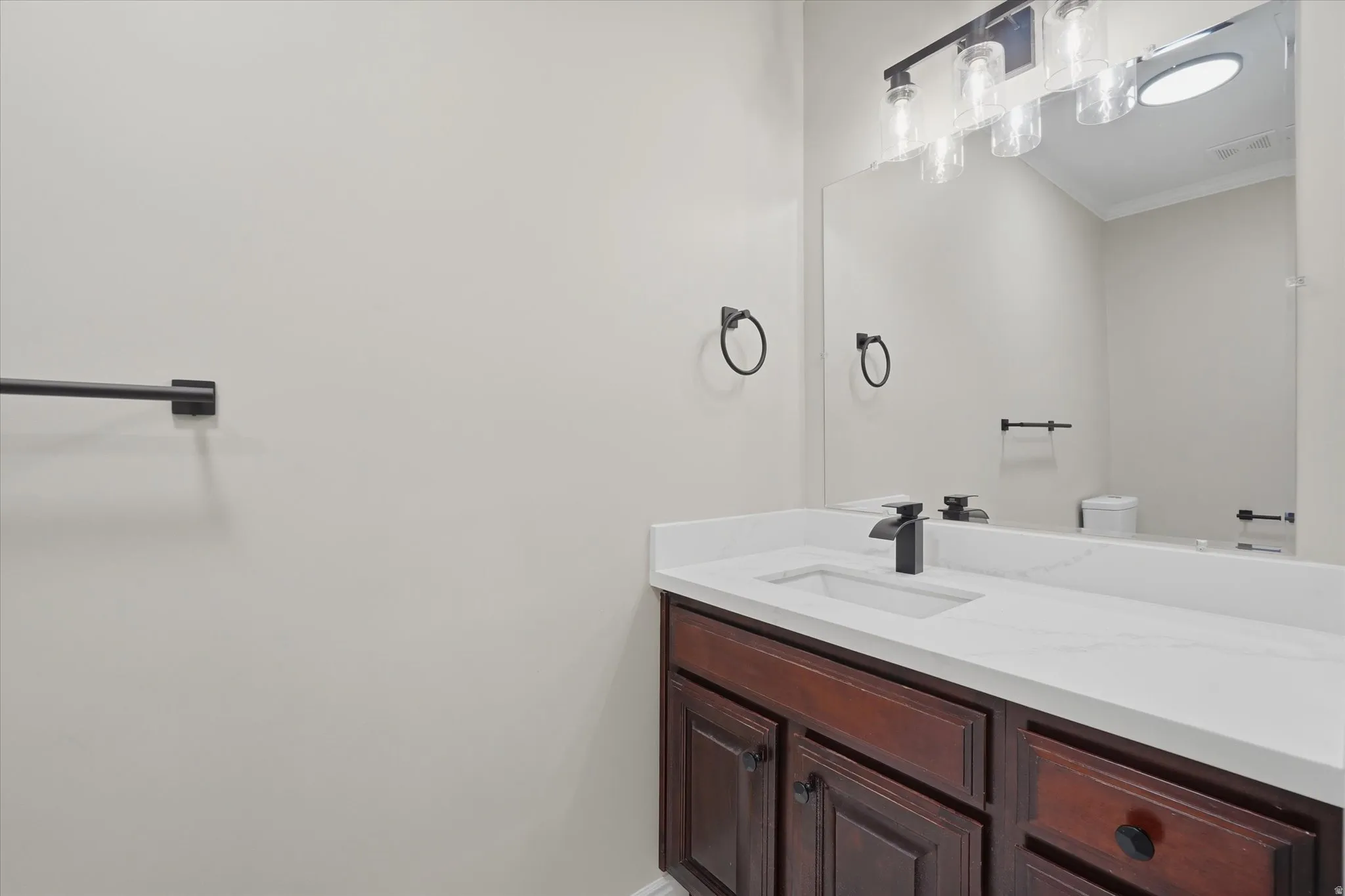 Bathroom vanity featuring a rich wood-finish cabinet with black hardware, a pristine white countertop, and a sink