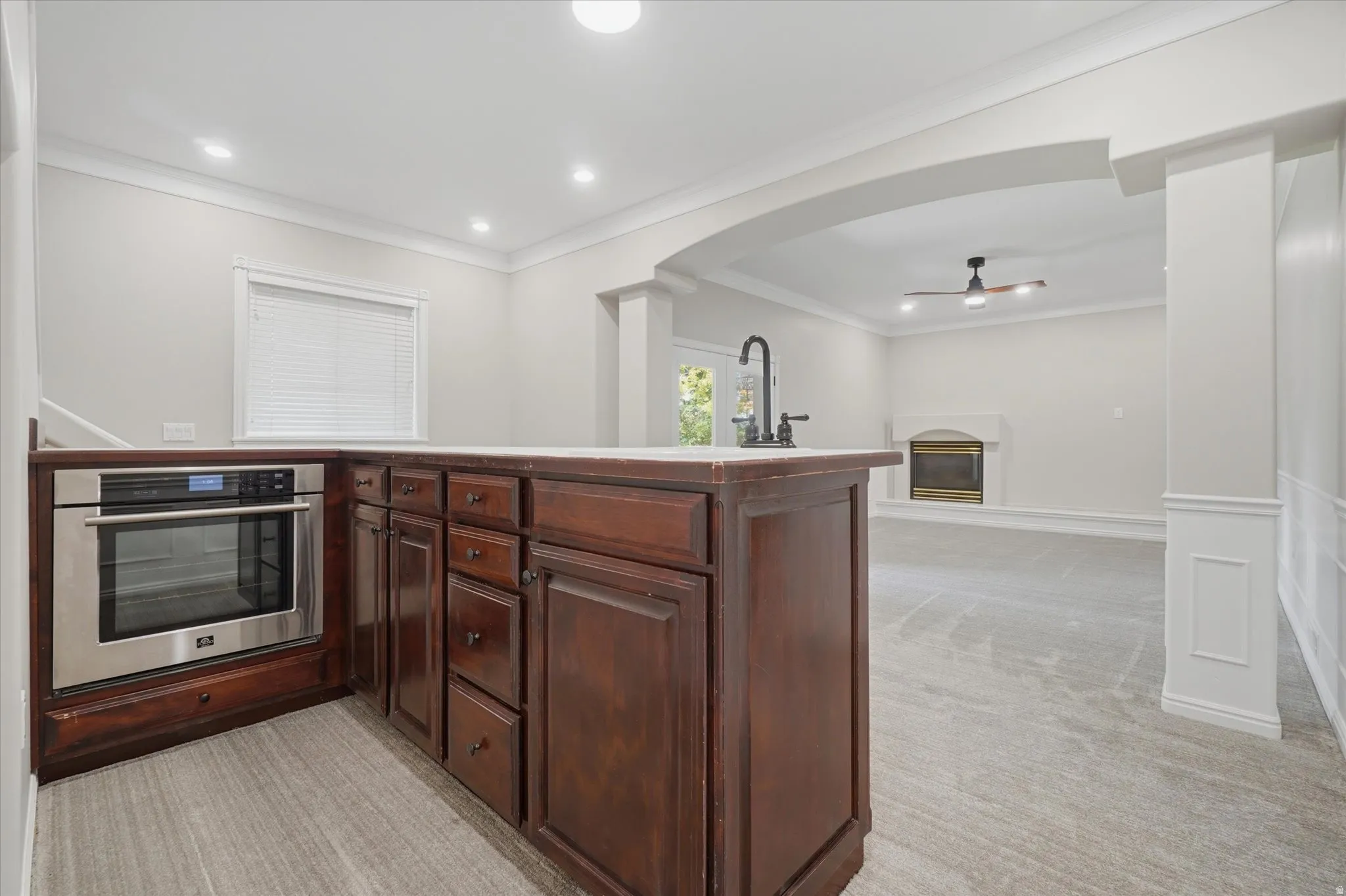 Kitchenette featuring built-in stainless steel oven, dark wood cabinetry with a light-toned countertop, and a matte black gooseneck faucet