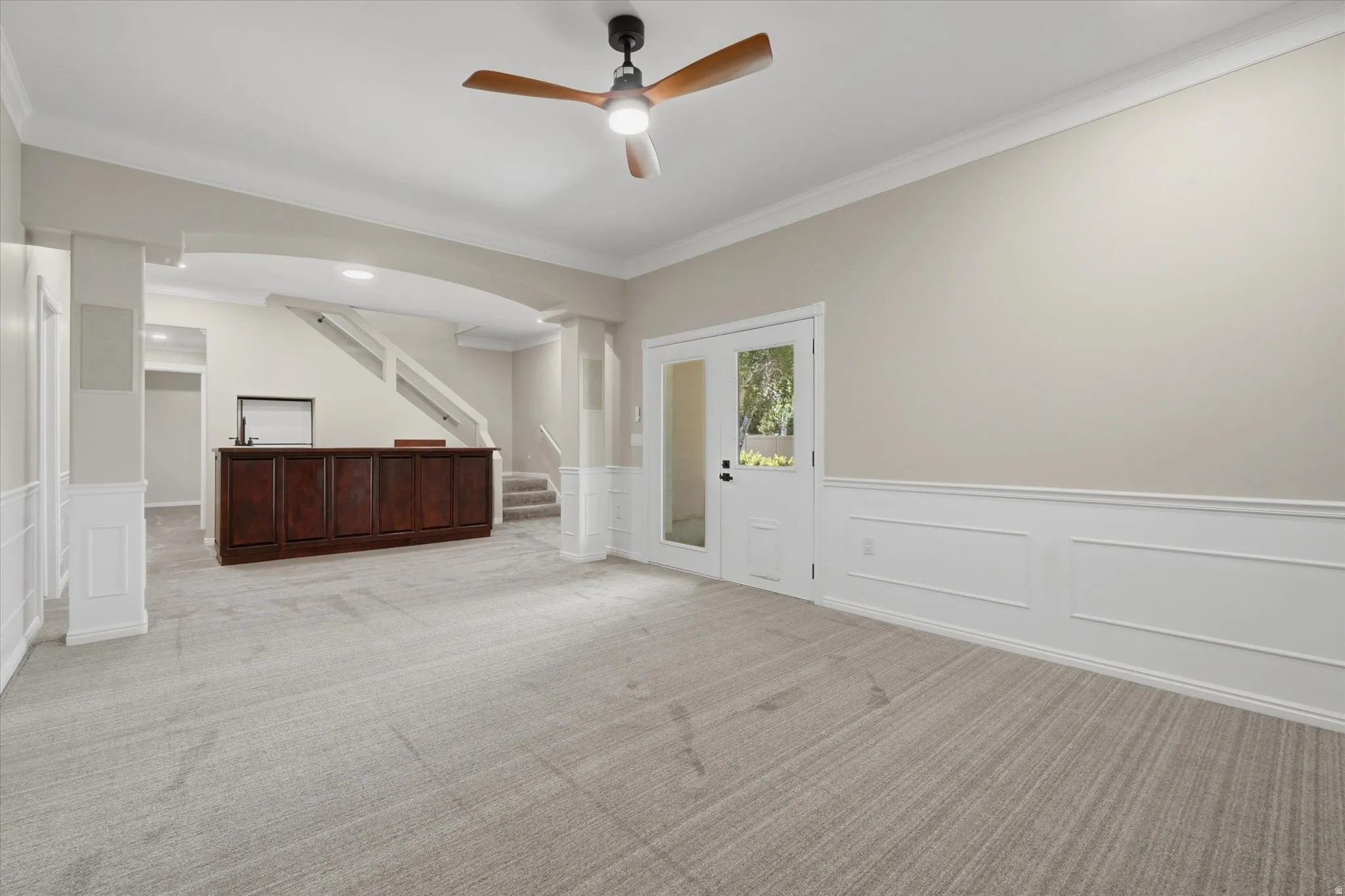 Spacious room featuring light-toned carpeting, wainscoting, and crown molding