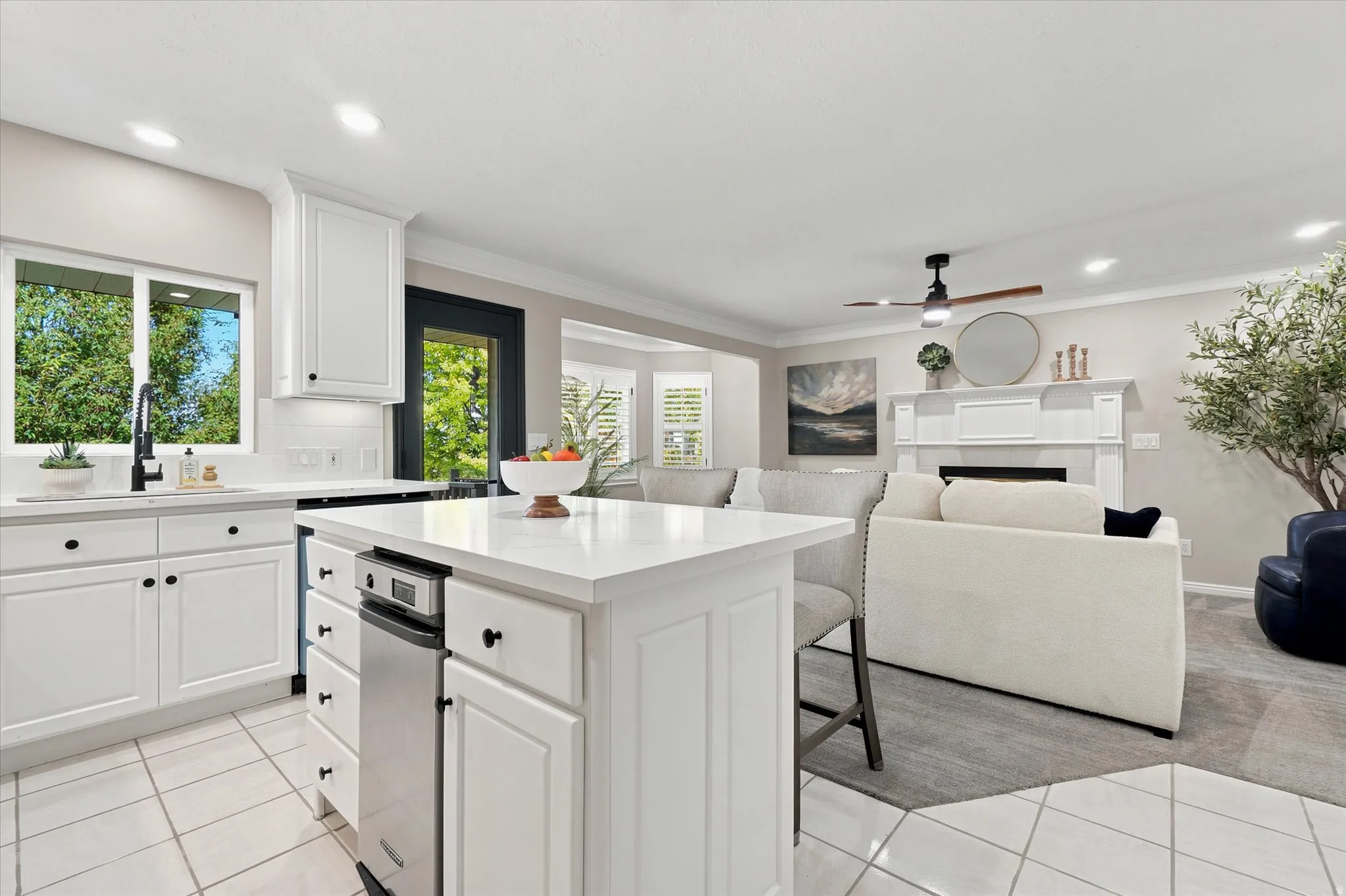 Open-concept kitchen and living area featuring white cabinetry, a kitchen island with integrated dishwasher, and a fireplace with a detailed mantel