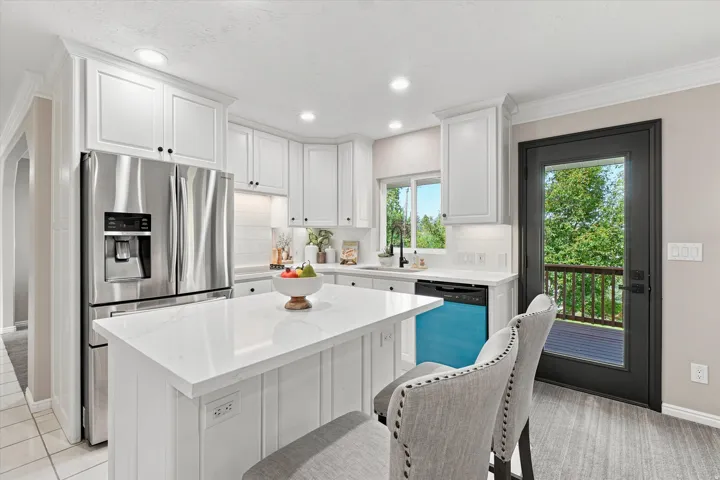 Modern kitchen featuring white cabinetry, a large center island with a stone-finish countertop, stainless steel appliances, and wood-finish flooring