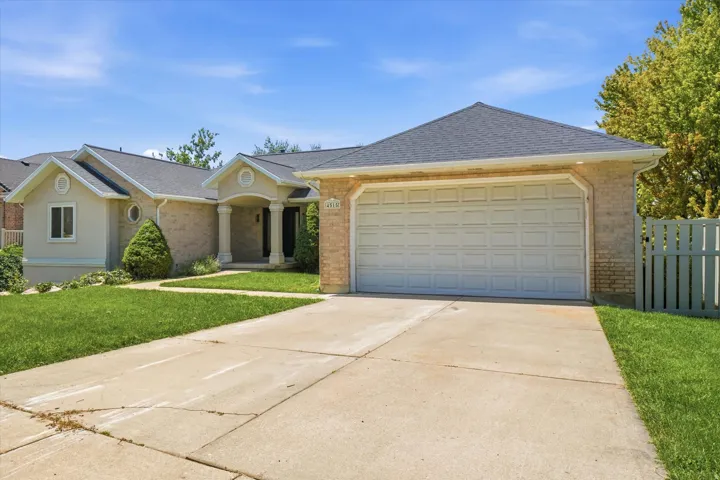 Brick and stucco facade featuring a two-car garage, a covered entry with columns, a dark shingle roof, and a concrete driveway