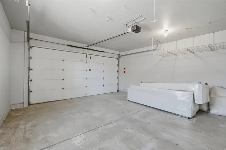 Spacious garage featuring a concrete floor, white panel garage door, and an automatic garage door opener and storage above.