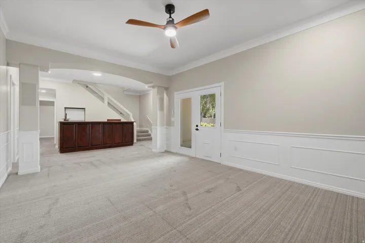 Spacious room featuring light-toned carpeting, wainscoting, and crown molding